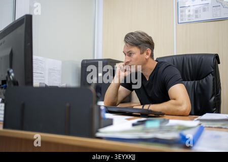 Thoughtful office worker resting his chin on his hand while looking at a computer screen. Brainstorming, problem solving, and work pause. Stock Photo