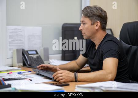 Professional man typing on a keyboard while looking at a computer monitor. Office work, data entry, and daily business routine. Stock Photo