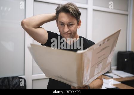 Concentrated worker studying paperwork. Man reading documents with puzzled expression in office. Stock Photo