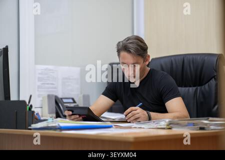 Focused businessman using a calculator and writing notes on financial documents. Profit calculation, accounting, and business analysis. Stock Photo