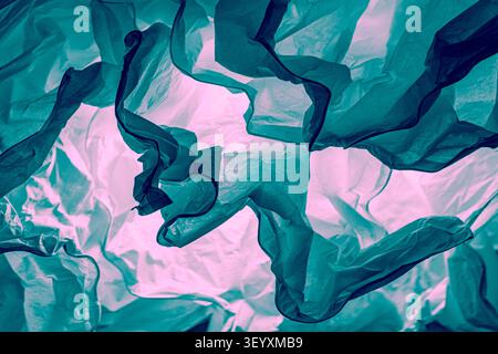 Close-up of crumpled translucent paper with colored back lighting. Textured background with pink neon light and turquoise folds in material. Stock Photo