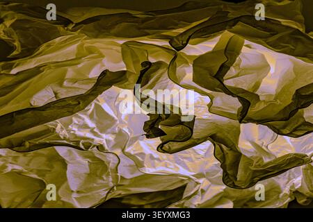Texture of badly crumpled thin material with creases. Abstract graphic pattern of tracing paper layers in contrasting mustard and white lighting. Stock Photo