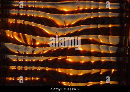 This image showcases a unique textured glass surface with warm, golden reflections, creating a captivating visual Stock Photo