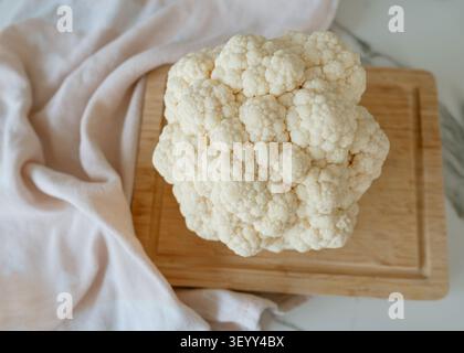A close-up of cauliflower on a wooden cutting board in a clean kitchen setting, captured from a top-down view, emphasizing the fresh and healthy Stock Photo