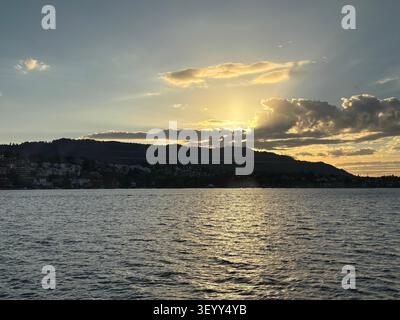 The sun setting behind the hills of Lake Zurich, casting a golden glow over the water ripples, Zurich, Switzerland Stock Photo
