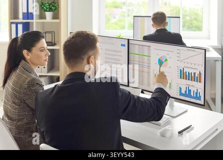 Colleagues discussing market data and strategy charts on computer monitors Stock Photo