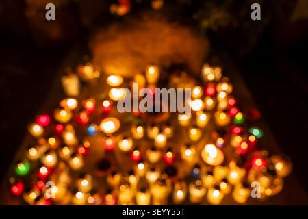Blurry out of focus soft abstract background filled with votive candle lights burning at night on cemetery tomb. Stock Photo
