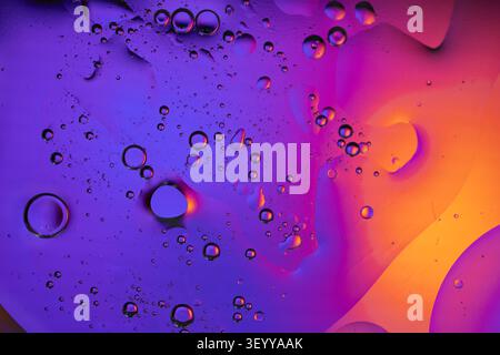 Oil drops on a vibrant purple and orange fluid surface creating abstract patterns Stock Photo