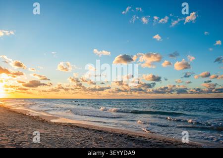 Sunset at the beach with calm waves and fluffy clouds in the sky. Stock Photo