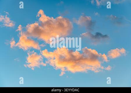 Beautiful clouds in a bright blue sky during sunset with warm hues of orange and pink. Stock Photo