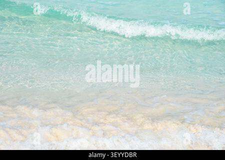 A sandy beach with clear turquoise water and small waves washing up on the shore. Stock Photo