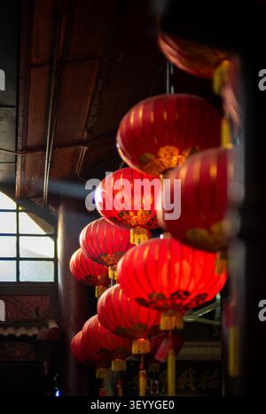 Low-angle perspective of traditional red Chinese lanterns with gold patterns hanging inside a temple, illuminated by a shaft of natural light Stock Photo