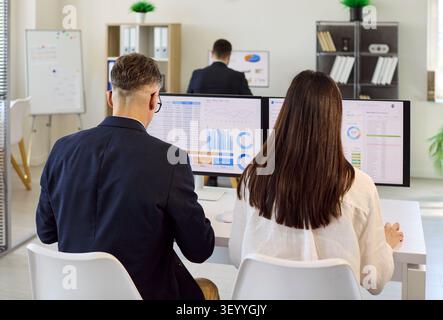 Analysts collaborating on finance dashboards at computers in modern bright office Stock Photo