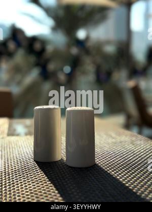 Close-up of a pair of minimalist white ceramic salt and pepper shakers on a woven placemat at an outdoor restaurant table Stock Photo
