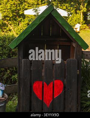 Rustic wooden garden tool house with painted red heart in a sunny garden Stock Photo