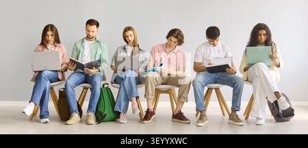 Diverse college students studying with laptops and notebooks against gray wall Stock Photo