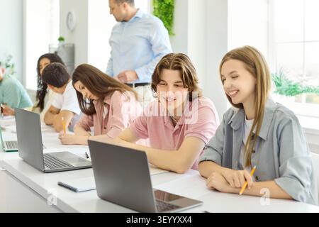 Smiling college students studying with laptops in classroom as teacher guides Stock Photo