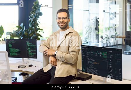 Confident male programmer in modern office with code on dual monitors and desk Stock Photo