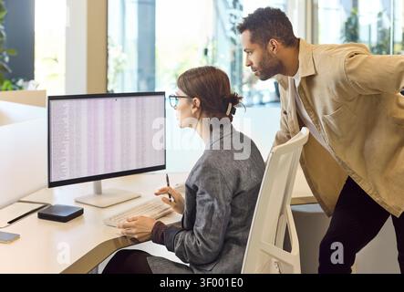 Colleagues analyzing spreadsheet on monitor during focused financial workflow Stock Photo