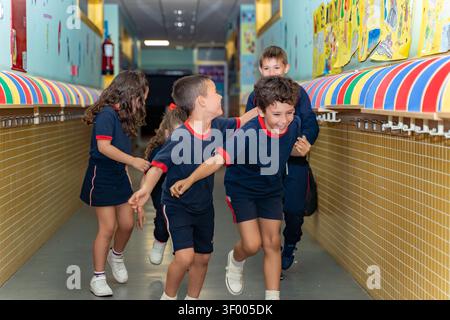 Cheerful students in uniform running and playing together, sharing laughter and joy in a vibrant school corridor Stock Photo