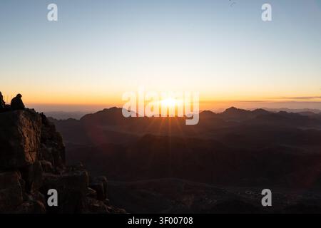 Sunrise over the Sinai desert view from mount Sinai after a long night trekking to the top sitting on a cliff ridge Stock Photo