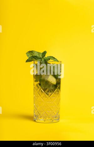 Refreshing mojito cocktail in a textured glass with lime slices and mint leaves on a bright yellow background. The clean composition and vivid color c Stock Photo