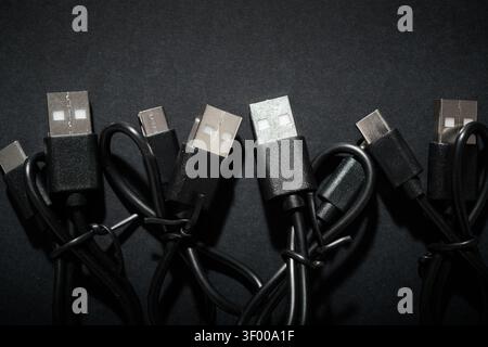 Close-up of a group of coiled black USB-C to USB-A cables. They are used for fast data transfer and charging of electronic devices. Network connectors Stock Photo