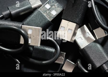 Close-up of a group of coiled black USB-C to USB-A cables. They are used for fast data transfer and charging of electronic devices. Network connectors Stock Photo