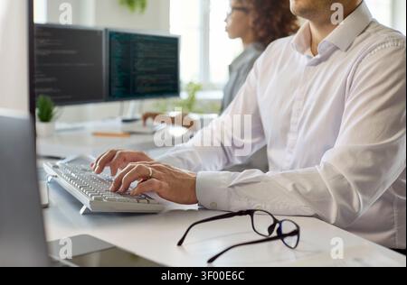 Closeup of software developer typing at keyboard in bright office, coding focus Stock Photo