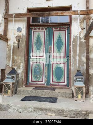 Tallinn, Estonia - 20 April 2024: Weathered painted wooden door with geometric patterns flanked by vintage lanterns Stock Photo