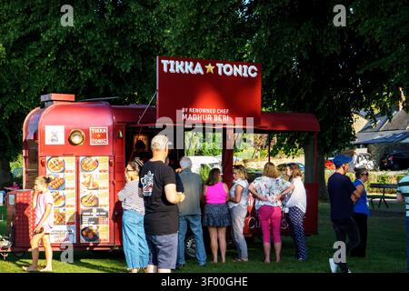 People queuing for takeaway food from a vibrant red food truck on a sunny day Stock Photo