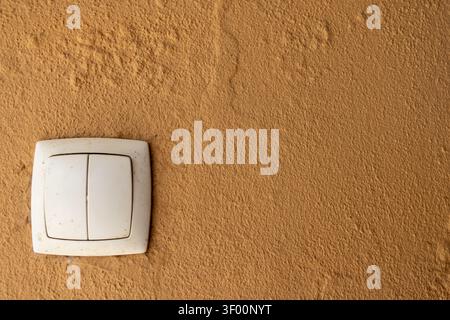A simple white double light switch is mounted on a rough, textured wall with a warm ochre color, creating a minimalist composition Stock Photo