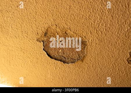 Detailed view of weathered ochre colored wall surface showing a patch of damaged plaster revealing rough concrete texture and cracks beneath Stock Photo