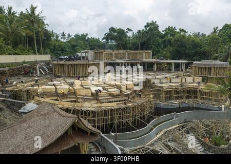 Aerial view of a large construction site featuring intricate bamboo scaffolding and concrete structures surrounded by lush tropical trees in Bali, Ind Stock Photo