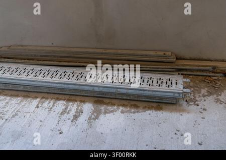Metal drainage grates and wooden planks are stored on a rough concrete surface at a building site Stock Photo
