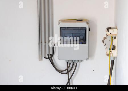 A close-up view of a residential electrical distribution box and a separate circuit breaker unit mounted on a textured white wall, showing conduit and Stock Photo