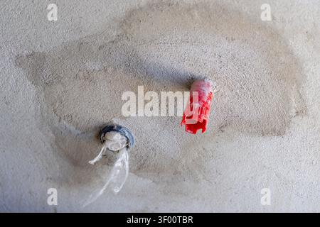 Two wall anchors, one red and one blue with plastic, are embedded in a rough concrete surface, suggesting construction or repair work Stock Photo