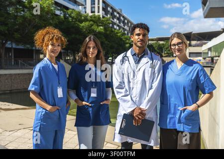 Diverse medical professionals including doctors and nurses smiling while standing together outside a modern clinic, representing teamwork, unity, and Stock Photo