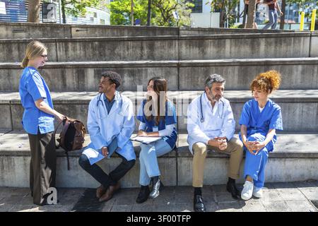 Diverse group of medical students and healthcare professionals collaborating outdoors, sitting on concrete steps, discussing medicine and education in Stock Photo