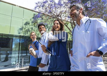 Diverse team of doctors and nurses walking and smiling outside a modern clinic, conveying teamwork, confidence, collaboration, happiness, and wellness Stock Photo