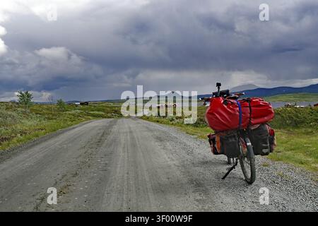 Bicycle with luggage on a dirt road under dramatic cloud formations, bicycle route, Jotunheimvegen, Mjolkevegen, Norway Stock Photo