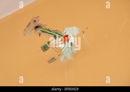 Close-up view of unfinished electrical work with wires and an orange junction box protruding from a hole in a textured wall Stock Photo