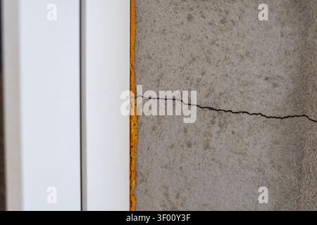 A detailed view of a structural crack in a concrete surface, bordered by bright yellow sealant and a clean white architectural element Stock Photo