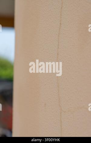 A detailed view of a rough, beige-colored exterior wall surface showing a fine hairline fracture running vertically Stock Photo