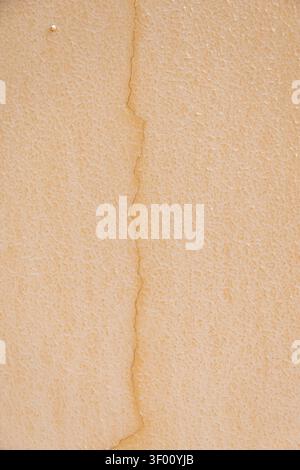 A detailed view of a rough, sandy-colored wall surface showing a prominent fissure, highlighting imperfections and texture Stock Photo