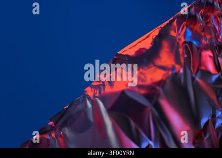 A striking abstract image featuring a crumpled metallic surface with vibrant red highlights, set against a rich, deep blue background, creating a vivi Stock Photo