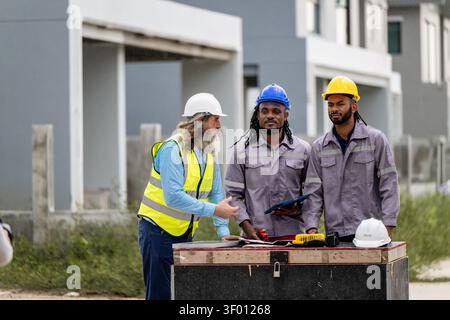 African American civil engineer holding walkie talkie and clipboard inspecting residential building site during daytime, scene for housing development Stock Photo