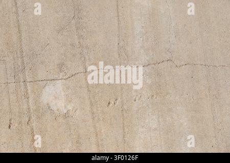 A detailed view of a light brown concrete wall showcasing its granular texture, faint vertical lines, and a prominent horizontal crack Stock Photo