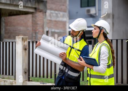 Project manager women and civil engineer wearing vests and hard hats inspect the quality of roofing materials, discussing details of material selectio Stock Photo