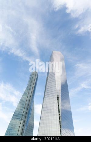 Low-angle view of two modern glass skyscrapers rising high into a bright blue sky with light clouds, showcasing contemporary architecture, business di Stock Photo